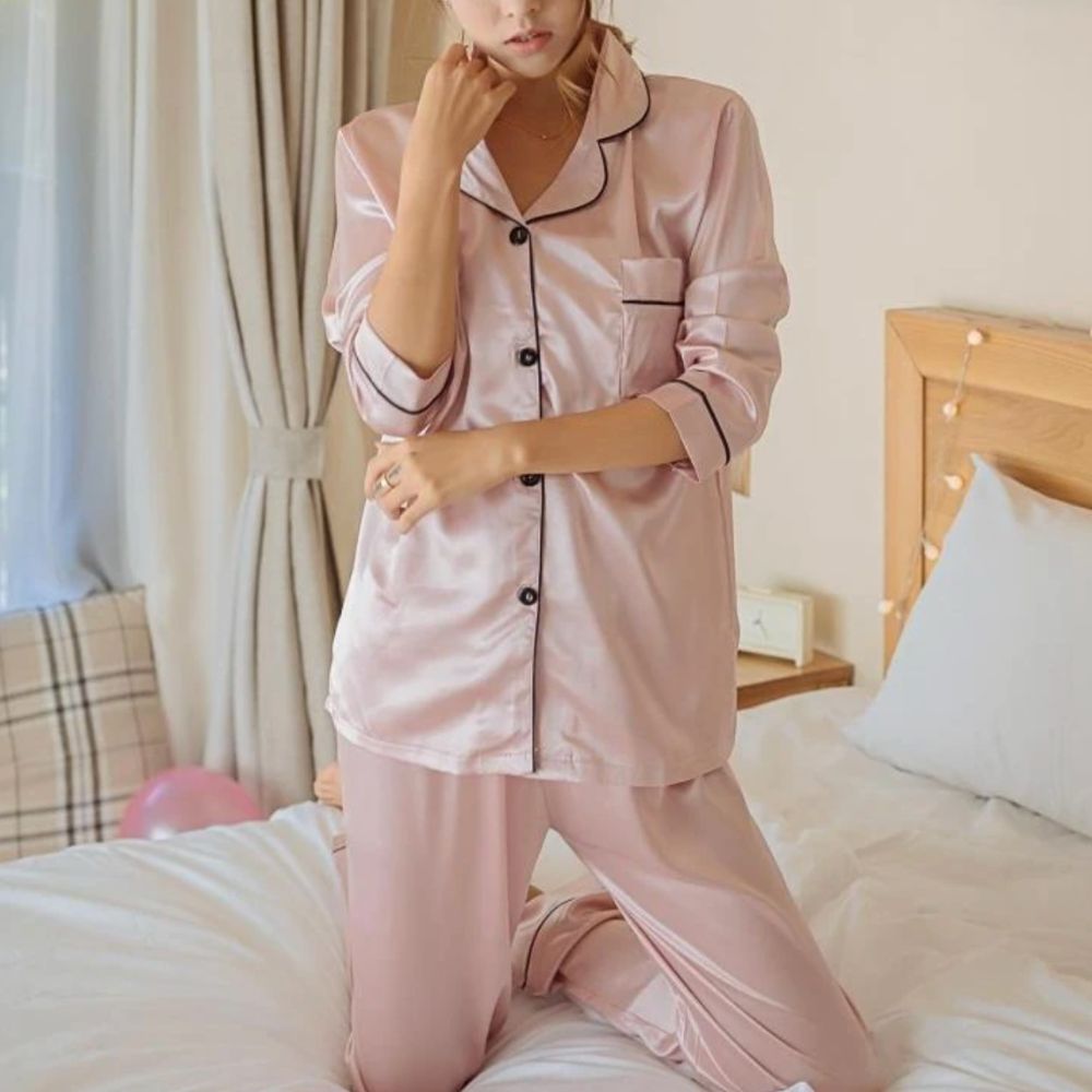 Woman in the pink satin pyjama set kneeling on a bed