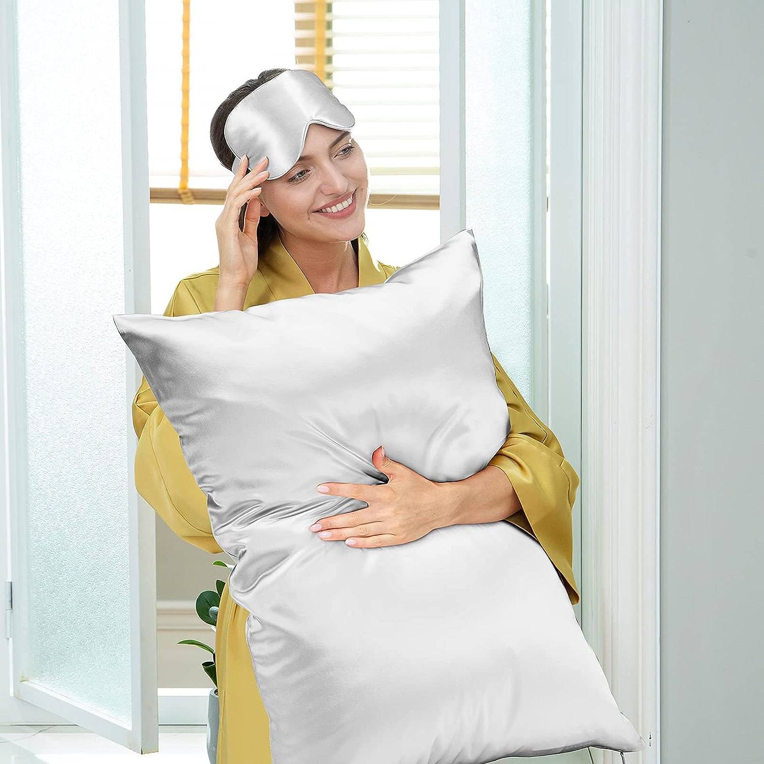 Woman holding a white mulberry silk pillowcase, wearing a silk eye mask